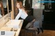 A woman in a white shirt and black skirt leaning over a sink.