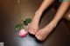 A woman's feet with a pink rose on the floor.