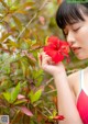 A woman in a red bathing suit smelling a red flower.