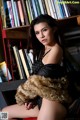 A woman sitting on a stool in front of a bookshelf.