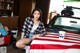 A woman sitting on top of a car covered in an American flag.