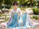 A woman in a blue and pink hanbok sitting on the ground.